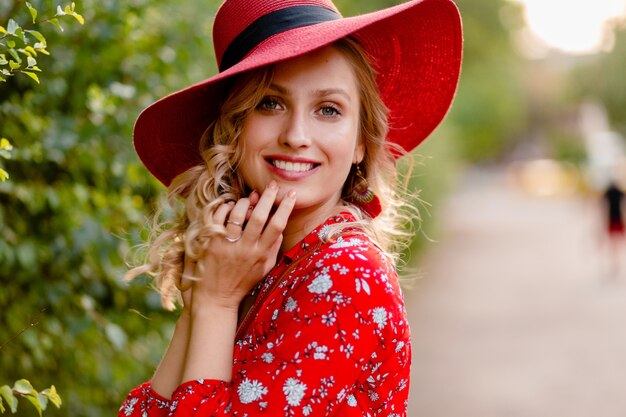 Retrato do close-up de uma mulher loira elegante e atraente sorridente com chapéu vermelho palha e blusa, roupa da moda de verão com estilo de cabelo encaracolado de sorriso