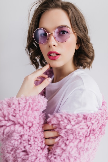 Retrato do close-up do encantador modelo feminino caucasiano em óculos de sol roxos. Mulher morena inspirada com cabelos ondulados.