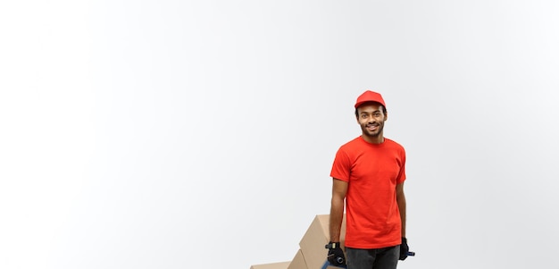 Retrato do conceito de entrega de um entregador afro-americano bonito ou mensageiro empurrando o caminhão de mão com pilha de caixas isoladas no espaço de cópia de fundo do estúdio cinza