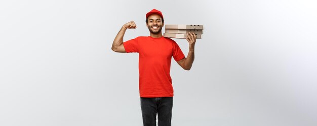 Retrato do conceito de entrega de um entregador afro-americano forte mostrando seu músculo com pacotes de caixa de pizza isolados no espaço de cópia de fundo do estúdio cinza