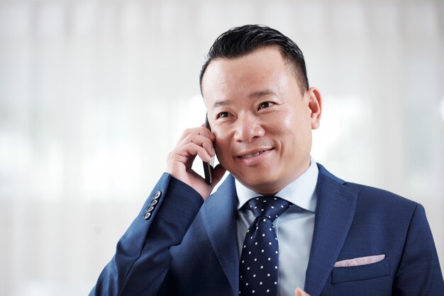 Retrato do empresário asiático tendo negociação por telefone com o parceiro de negócios
