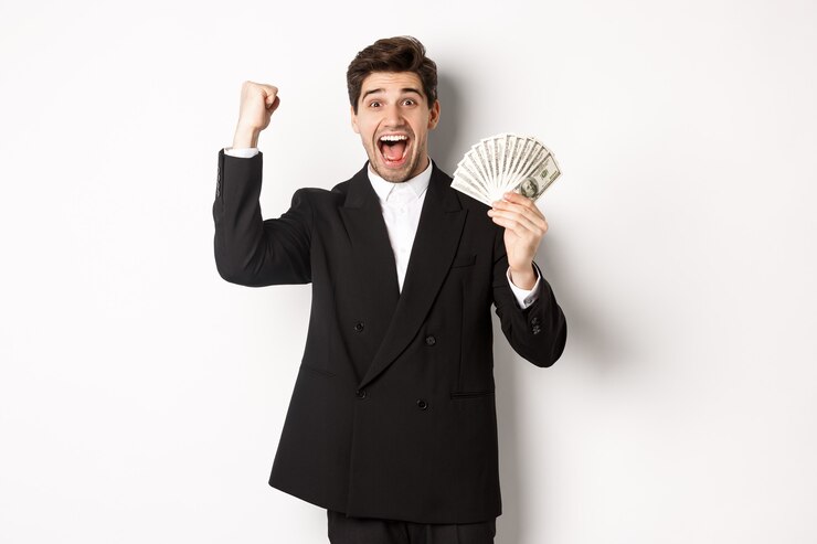 Foto grátis retrato do empresário bonito em terno preto, ganhando dinheiro e regozijando-se, levantando a mão com entusiasmo, de pé contra um fundo branco.
