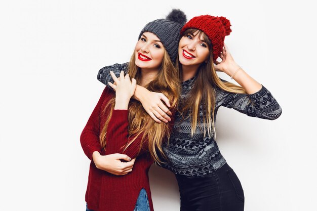 Retrato do estilo de vida interior de duas mulheres muito felizes, melhores amigas com chapéus de malha fofos e suéteres aconchegantes se divertindo