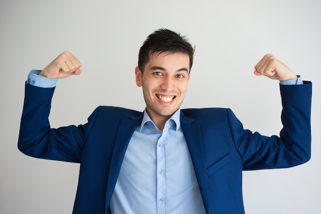 Retrato do homem de negócios caucasiano novo alegre que mostra os músculos.