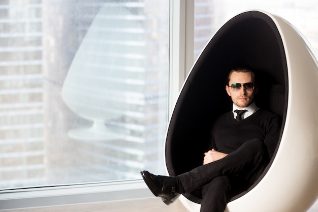 Retrato do homem misterioso à moda na cadeira futurista do ovo.