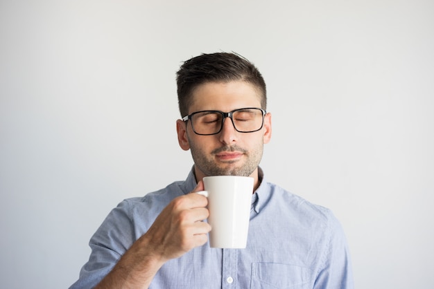 Retrato do homem nos monóculos que aprecia o café com olhos fechados.