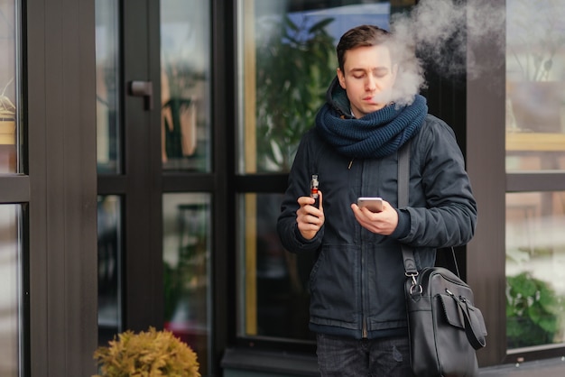 Foto grátis retrato do homem que vaping um atomizador ao ar livre. fumar seguro.