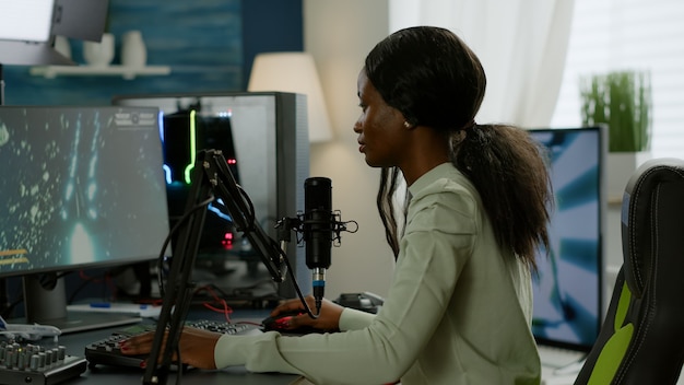 Retrato do jogador africano concentrado, olhando para a câmera sorrindo, jogando videogame de atirador espacial online para torneio de jogos. Cyber desempenho em um PC poderoso com videogames de streaming de teclado RGB