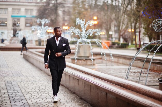 Retrato do jovem e bonito empresário americano africano de terno andando no cemitério da cidade com guirlandas
