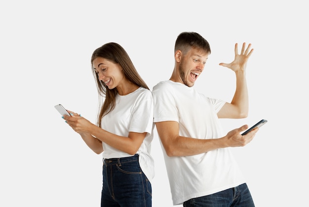 Retrato do lindo casal jovem isolado no fundo branco do estúdio. expressão facial, emoções humanas, conceito de publicidade. homem e mulher segurando smartphones e parecem loucamente felizes, comemorando.