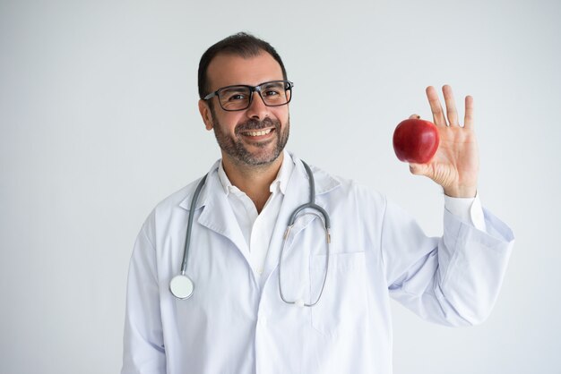 Retrato do médico geral adulto meados de feliz que guarda a maçã.