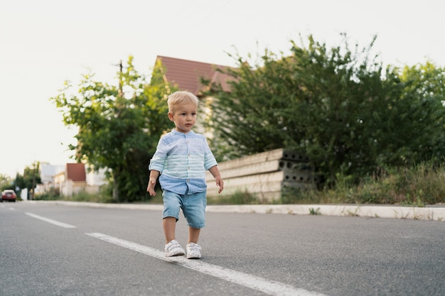 Retrato do menino bonitinho andando na estrada em seu bairro