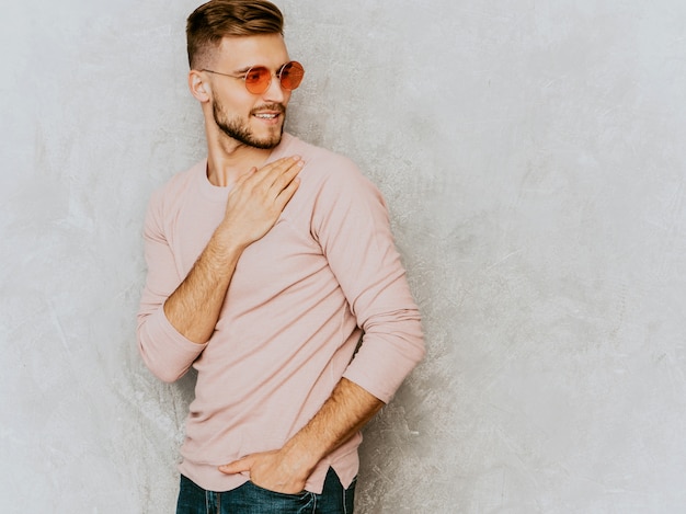 Retrato do modelo bonito jovem sorridente, vestindo roupas de verão casual rosa. moda elegante homem posando em óculos de sol redondos