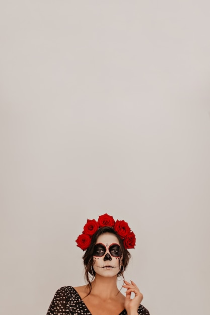 Retrato do modelo contra uma parede branca, posando em coroa de flores naturais. a maquiagem do esqueleto do halloween parece incomum