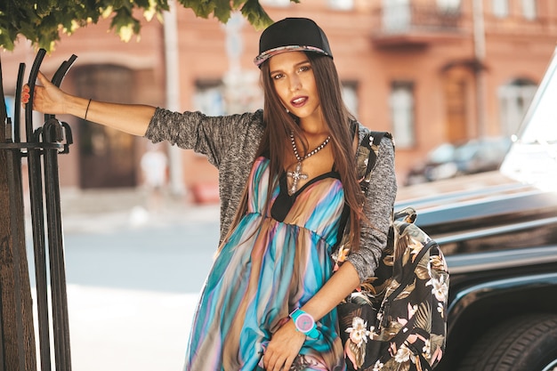 Retrato do modelo de adolescente morena glamour linda em roupas de verão hipster e bolsa. garota posando na rua. mulher de boné