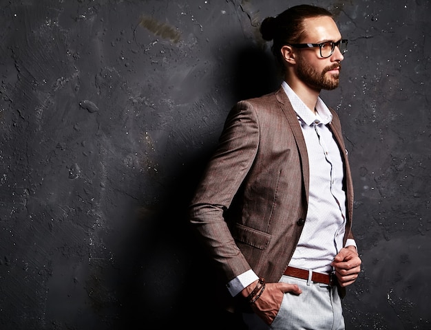 Foto grátis retrato do modelo de empresário de moda hipster elegante bonito vestido com elegante terno marrom em copos perto da parede escura