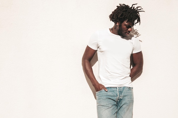 Retrato do modelo de hipster bonito sorridente Homem africano não barbeado vestido com camiseta branca de verão e jeans Moda masculina com penteado dreadlocks posando no fundo da rua