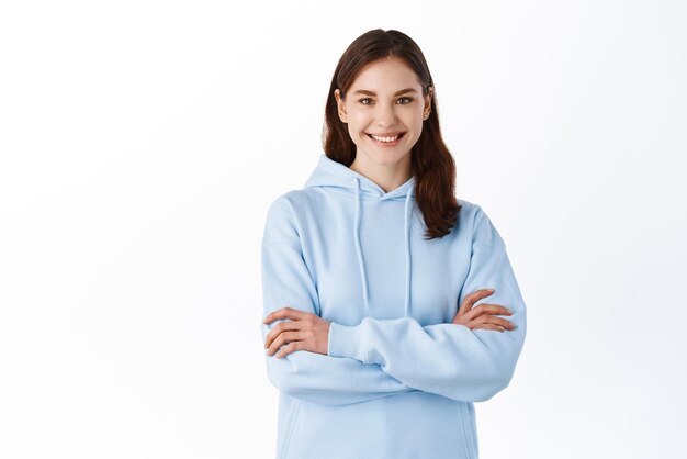 Retrato do modelo de menina feliz sorridente cruza os braços no peito vestindo roupas casuais mostrando expressão facial positiva e confiante em pé contra o fundo branco