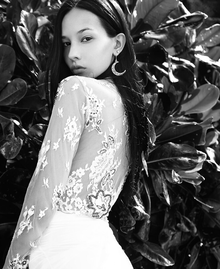 Foto grátis retrato do modelo de mulher bonita caucasiano com cabelos longos escuros nas calças clássicas de pernas largas posando perto de fundo verde tropical folhas exóticas