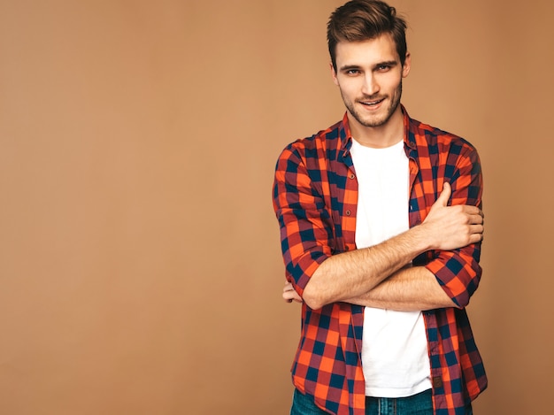 Retrato do modelo elegante jovem sorridente bonito vestido com camisa quadriculada vermelha. homem moda posando. braços cruzados