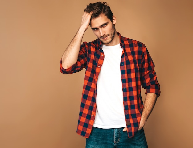 Retrato do modelo elegante jovem sorridente bonito vestido com camisa quadriculada vermelha. Homem moda, posar