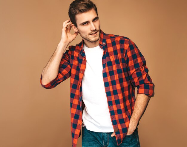 Retrato do modelo elegante jovem sorridente bonito vestido com camisa quadriculada vermelha. Homem moda, posar