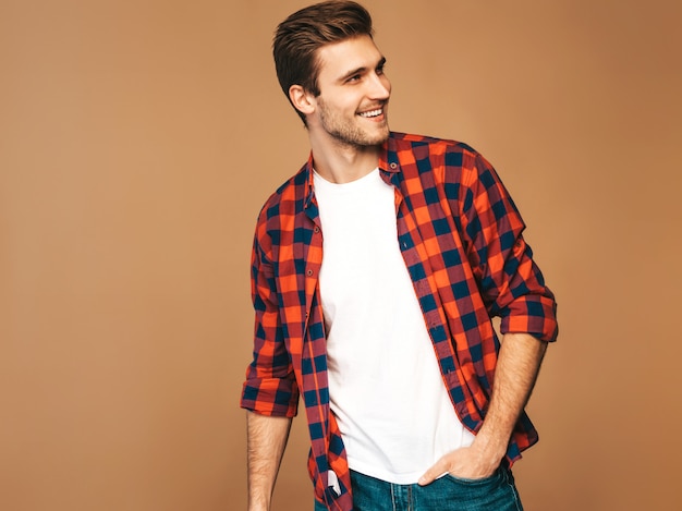 Retrato do modelo elegante jovem sorridente bonito vestido com camisa quadriculada vermelha. Homem moda, posar