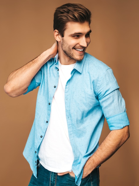 Retrato do modelo elegante jovem sorridente bonito vestido com roupas de camisa azul. Homem moda, posar