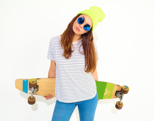 Foto grátis retrato do modelo jovem elegante em roupas de verão casual com chapéu gorro amarelo posando com mesa de longboard. isolado no branco