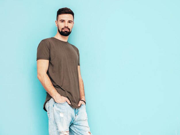 Retrato do modelo lambersexual bonito e elegante hipster homem vestido de camiseta e jeans Moda masculina isolada na parede azul no estúdio