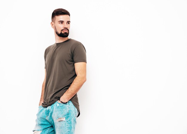 Retrato do modelo lambersexual bonito e elegante hipster homem vestido de camiseta e jeans Moda masculina isolada na parede branca no estúdio