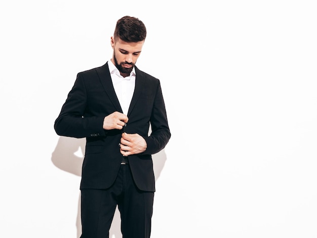 Retrato do modelo lambersexual elegante hipster confiante bonito Homem moderno sexy vestido com terno preto elegante Moda masculina posando no estúdio perto da parede branca isolada