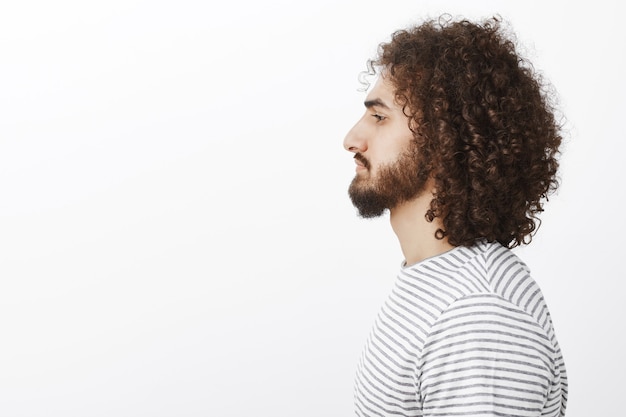 Retrato do perfil de um cara hispânico bonito com barba e cabelo encaracolado, olhando para o lado sem emoções.