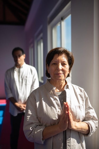 Retrato do treinador de ioga asiático de conteúdo no ginásio. Mulher sênior na camisa de mãos dadas em Namastê. Conceito de meditação