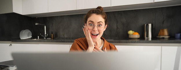 Retrato em close-up de jovem surpreendida olhando para o laptop com expressão de rosto feliz e surpresa