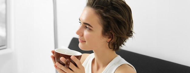 Foto grátis retrato em close-up de mulher relaxada descansando na cama acordando e bebendo uma xícara de café pela manhã