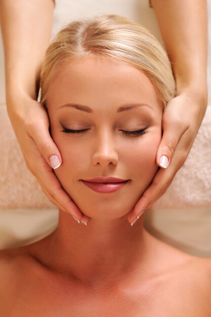 Retrato em close-up de um rosto feminino bonito recebendo massagem relaxante na cabeça