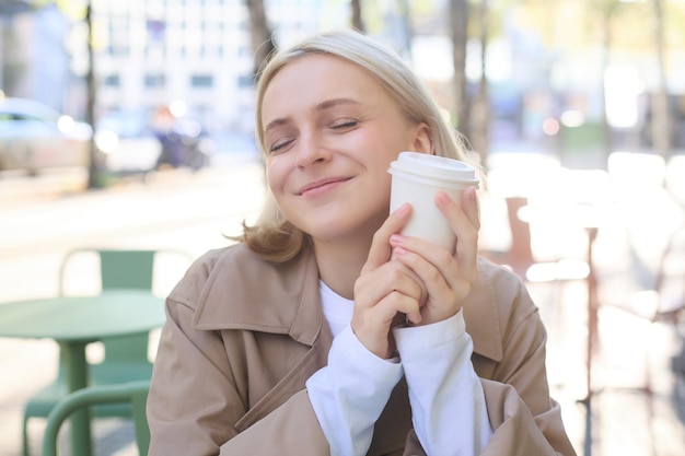 Foto grátis retrato em close-up de uma bela mulher europeia sorridente, feliz, sentada num café e a desfrutar de uma chávena de