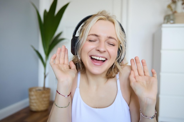 Retrato em close-up de uma jovem feliz e sincera com fones de ouvido cantando e ouvindo música em casa