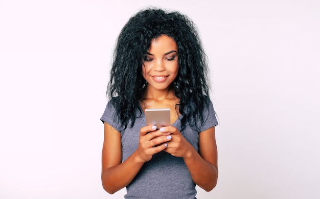 Retrato em close-up de uma mulher afro com sorriso largo e atraente e cabelo comprido e crespo, que expressa felicidade ao ler algo em seu smartphone