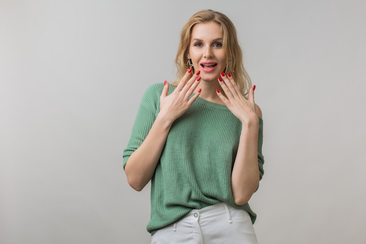 Foto grátis retrato emocional de uma jovem atraente surpresa com expressão de choque no rosto, boca aberta, mãos para cima, emoção engraçada, estilo casual, suéter verde, louco, isolado, olhando na câmera