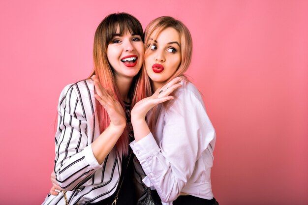 Retrato engraçado de duas garotas felizes e surpresas se divertindo muito juntas e fofocando, com roupas legadas em preto e branco