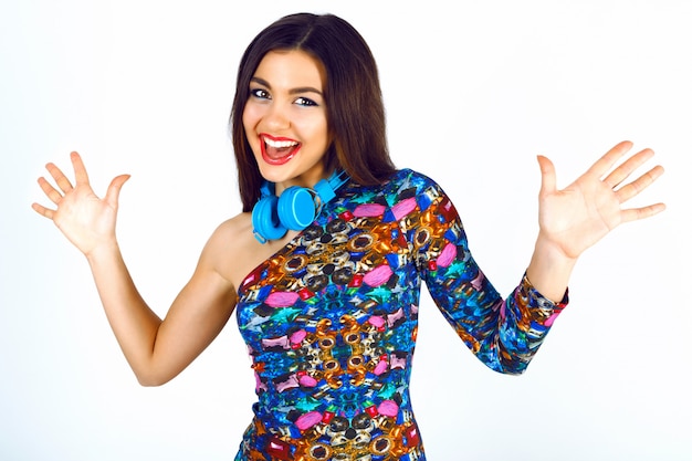 Foto grátis retrato engraçado do estilo de vida de uma mulher bonita em um vestido de festa elegante e brilhante e grandes fones de ouvido azuis, se divertindo, emoções positivas.