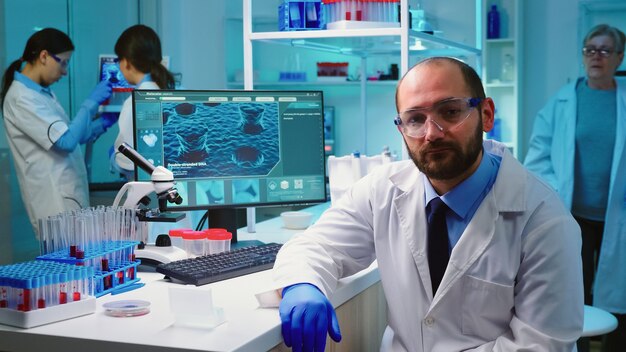 Retrato exausto de um médico químico olhando para uma câmera de vídeo sentado em um laboratório equipado, trabalhando tarde da noite