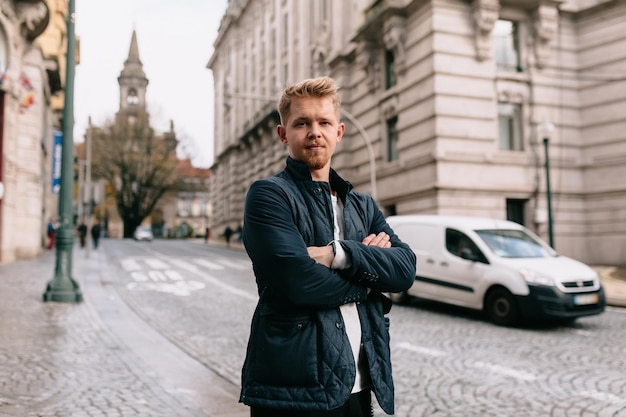 Retrato externo de jovem bonito com cabelos loiros e olhos azuis vestindo jaqueta azul está olhando para a câmera na rua europeia em dia ensolarado de primavera quente