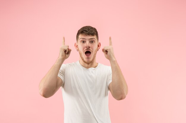 Retrato frontal de meio comprimento masculino atraente em estúdio rosa backgroud. Homem barbudo surpreso emocional jovem em pé com a boca aberta.