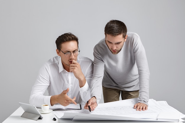 Retrato horizontal de arquitetos ocupados e intrigados tentando entender esboços, apontar com caneta,