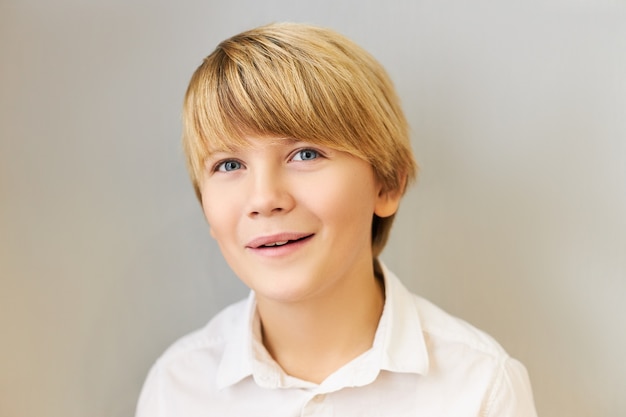 Retrato horizontal de atraente estudante caucasiano de olhos azuis com penteado elegante, sorrindo alegremente, tendo encantado a expressão facial animada, fascinado com algo incrível. Emoções positivas