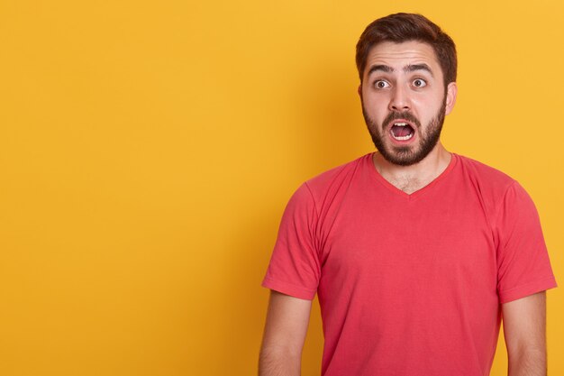 Retrato horizontal de homem morena atônito, vestindo camisa casual vermelha, posa contra amarelo