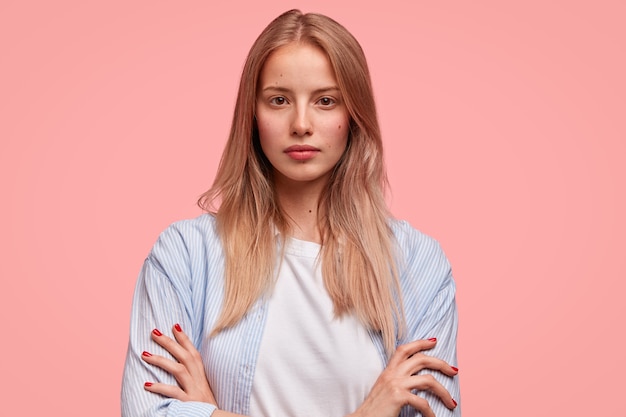 Retrato horizontal de mulher europeia séria e atraente com as mãos cruzadas e parece confiante